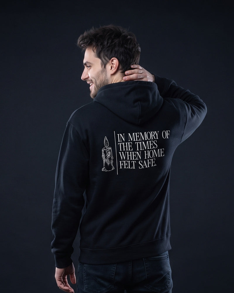 Mann trägt den WORN OPINIONS Hoodie In memory of the times in Schwarz von hinten, Rückenprint In memory of the times when home felt safe mit Kerzen-Illustration
