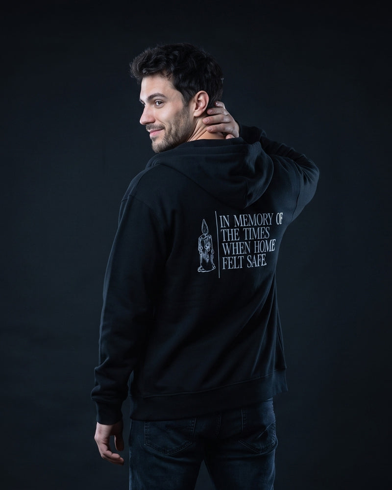 Mann von hinten in schwarzem Zip-Hoodie mit Kerzen-Illustration und dem Schriftzug 'In memory of the times when home felt safe.'