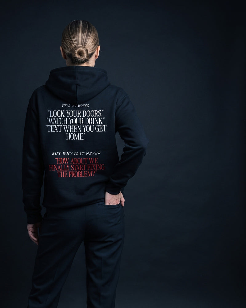 Frau in schwarzem Hoodie, Rueckenprint mit mehreren Zitaten in Anfuehrungszeichen und roter Schlusszeile "How about we finally start fixing the problem?"