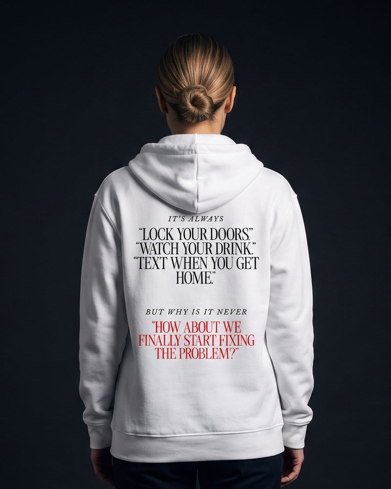 Frau in weißem Zip-Hoodie von hinten, Rückenprint „It's always ‚Lock your doors.‘ ‚Watch your drink.‘ ‚Text when you get home.‘ But why is it never ‚How about we finally start fixing the problem?‘“