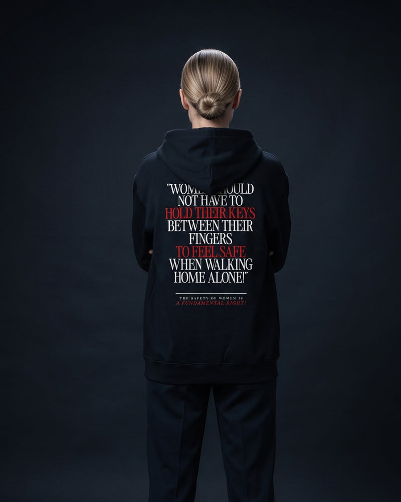 Frau von hinten im schwarzen Zip-Hoodie mit dem Rueckenprint "Women should not have to hold their keys between their fingers to feel safe when walking home alone! The safety of women is a fundamental right!"