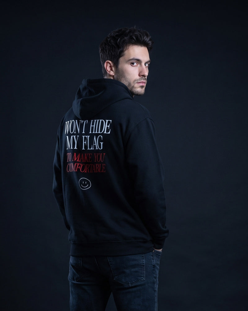 Mann von hinten in schwarzem Hoodie mit dem Aufdruck "WON'T HIDE MY FLAG" und darunter kursiv-rot "TO MAKE YOU COMFORTABLE" samt kleinem Smiley-Icon.