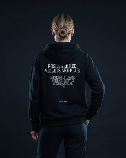 Frau in schwarzem Zip-Hoodie mit Rueckenprint: Gedicht 'Roses are red, violets are blue. Apparently loving your country is controversial too.' und kursiver Schlusszeile '- END OF POEM -'