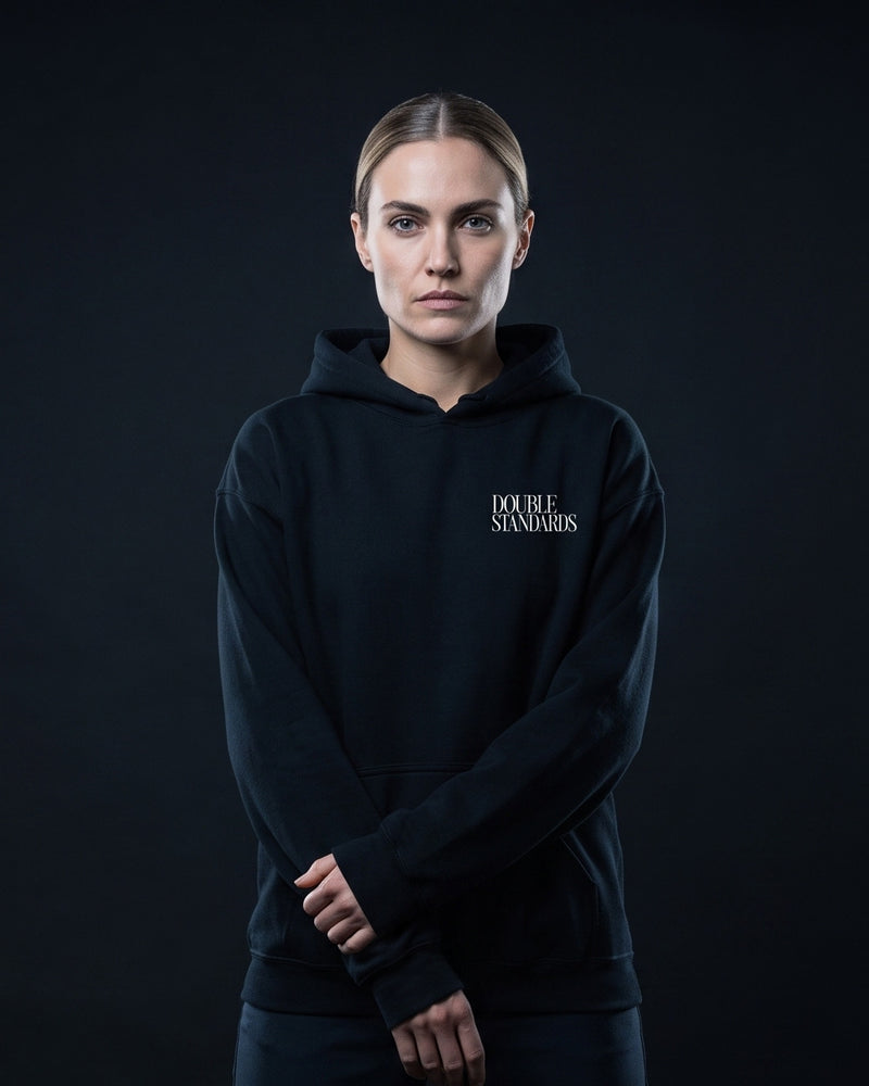Frau in schwarzem Hoodie mit dem Print 'DOUBLE STANDARDS' auf der Brust