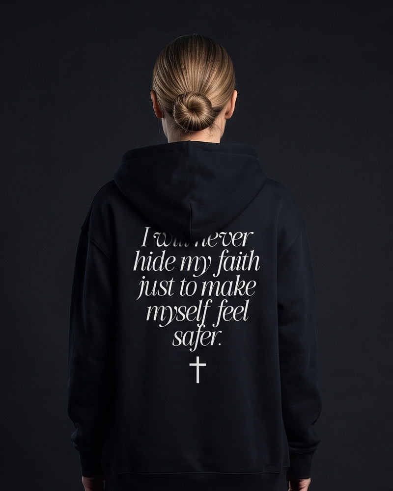 Frau in schwarzer Zip-Hoodie mit Rueckenprint 'I will never hide my faith just to make myself feel safer.' und einem Kreuz-Symbol darunter