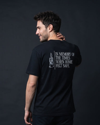 Mann trägt das WORN OPINIONS T-Shirt In memory of the times in Schwarz von hinten, Rückenprint In memory of the times when home felt safe mit Kerzen-Illustration
