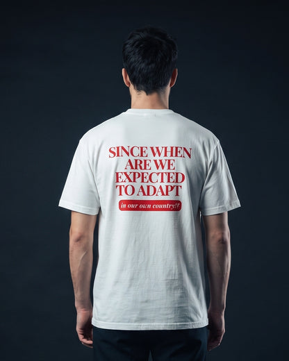 Mann von hinten in weissem T-Shirt mit dem Aufdruck 'Since when are we expected to adapt in our own country!?'