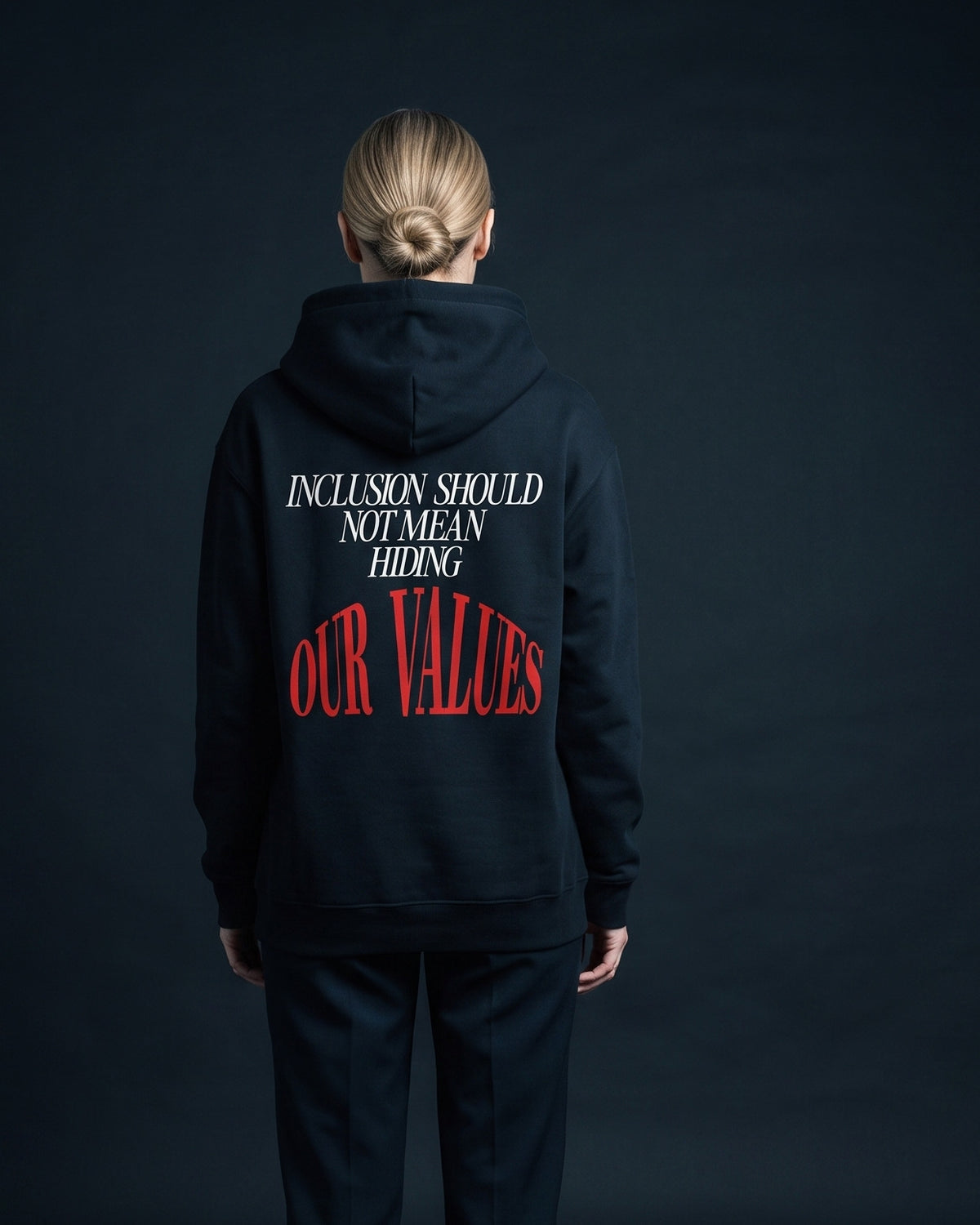 Frau traegt den WORN OPINIONS Hoodie Inclusion should not mean hiding our values in Schwarz von hinten, Rueckenprint Inclusion should not mean hiding, unten rot OUR VALUES