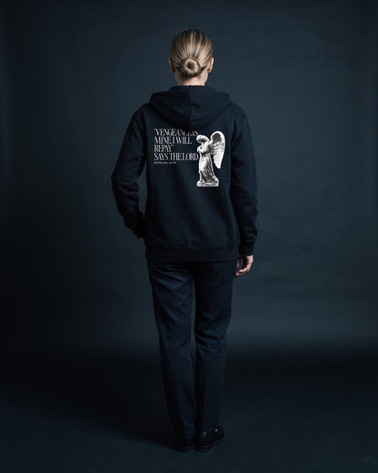 Schwarzer Zip-Hoodie mit Rueckenprint "Vengeance is mine, I will repay," says the Lord, Roemer 12:19, neben einer Engelsstatue