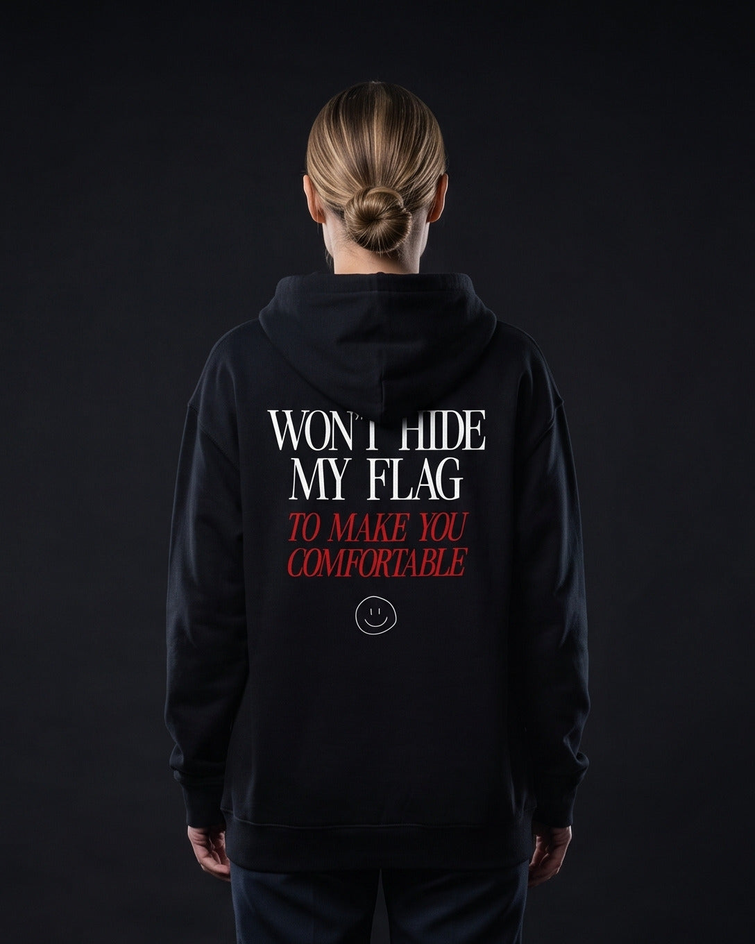 Frau von hinten in schwarzem Zip-Hoodie mit dem Aufdruck "WON'T HIDE MY FLAG" und darunter kursiv-rot "TO MAKE YOU COMFORTABLE" samt kleinem Smiley-Icon.