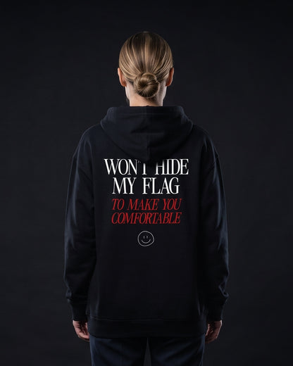 Frau von hinten in schwarzem Zip-Hoodie mit dem Aufdruck "WON'T HIDE MY FLAG" und darunter kursiv-rot "TO MAKE YOU COMFORTABLE" samt kleinem Smiley-Icon.
